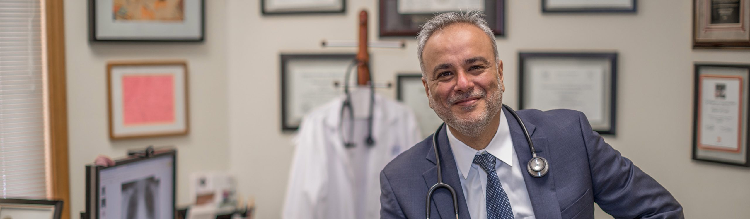 Dr. Saud Anwar in his medical office, wearing a stethoscope