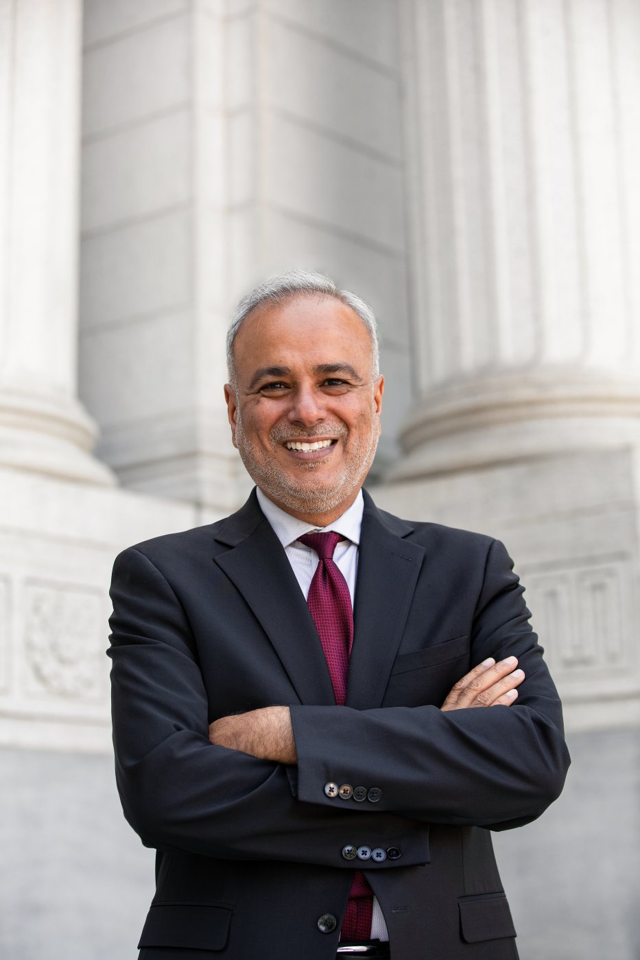 Portrait of Dr. Saud Anwar, arms crossed, before stone columns